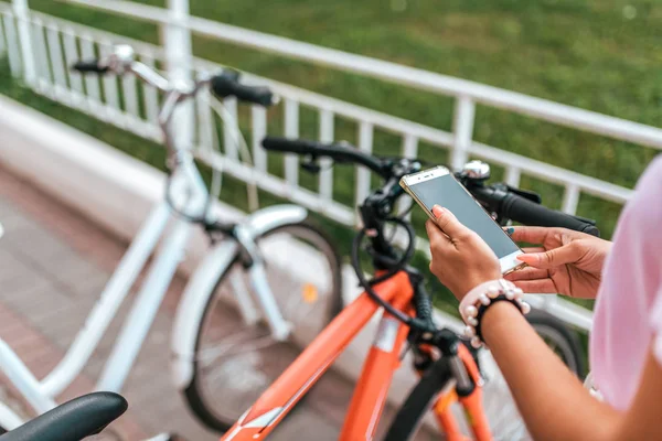 Di kota musim panas latar belakang sepeda parkir, gadis memilih aplikasi rute, internet online map phone. Rute jalur sepeda. Kota parkir sepeda. Penyewaan dan pemblokiran, aplikasi proteksi Internet . — Stok Foto