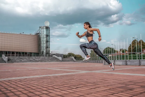 Жінка стрибає спортсменка-дівчина навушники з телефоном слухає музику, в той час як біг літнє місто, спортивний одяг легінси зверху. Вільний простір. Концепція здорового способу життя, мотивація. Емоції впевненість сила швидкість . — стокове фото