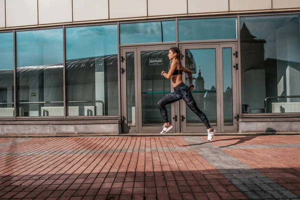 A woman runs in city in summer, a girl athlete runs, sportswear leggings top sneakers. Free space. The concept of a healthy lifestyle, motivation. Emotions of self-confidence, strength and speed.