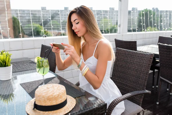 Mädchen nimmt Cocktail mit Zitrone. im Sommer an einem Cafétisch. Ruhe nach der Arbeit zum Mittagessen im Restaurant. In einem Café im Freien wartet man auf die Bestellung eines Mittagessens. Cocktaillimonade mit Zitrone und Stroh. — Stockfoto