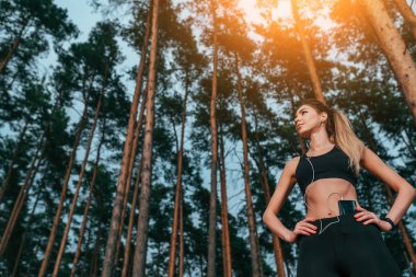 Arka plan ağaçları üzerinde güzel kız yaz parkı. Spor giyim, koşu ve temiz hava yürüyüş. Telefonla kulaklık müzik. Metin için boş alan. Kavram sağlıklı yaşam tarzı. Güven duyguları.