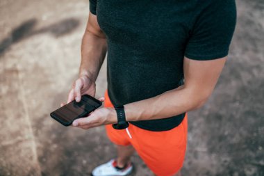 Erkek bir atletin elini yakın. Akıllı telefon, spor için uygulama seçimi. Şehirde yazın. Spor şort ve t-shirt giymek. Online fitness uygulamaları kavramı, spor nabız ve egzersiz süresi.