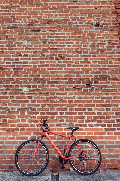 벽돌 오래된 벽의 배경에 빨간 자전거입니다. 텍스트의 여유 공간입니다. 주차 및 버려진 자전거의 개념. 자전거 프레임에 케이블을 잠그고 주차하십시오. 도시에서 여름에. — 스톡 사진