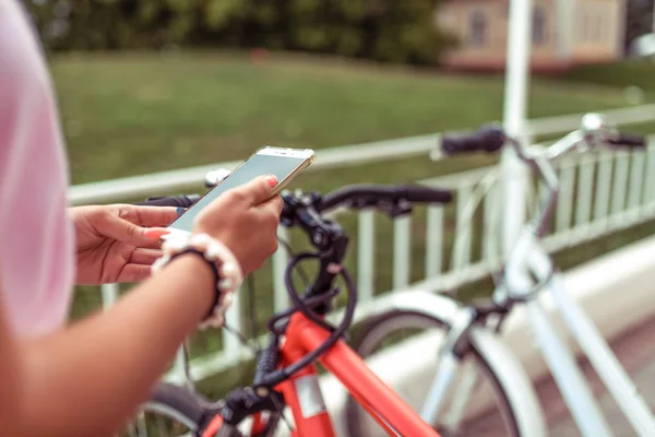 Gadis memilih rute kota smartphone musim panas. Sepeda parkir kota musim panas. Sepeda untuk disewakan. Aplikasi online ke Internet, pemesanan kendaraan, mengunci sepeda. Terhadap latar belakang parkir sepeda . — Stok Foto