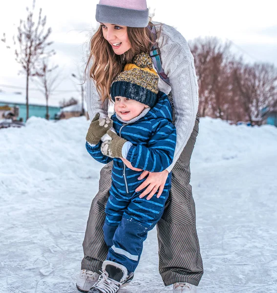Счастливая девочка-сестра играет с маленьким мальчиком-братом. Зимой на улице на фоне снега катаются на коньках по льду. В зимней одежде, отдых в новогодние праздники . — стоковое фото