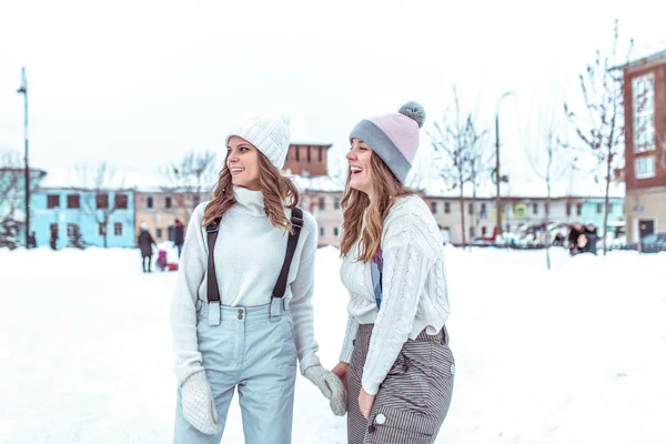 Dos amigas en invierno divirtiéndose al aire libre, en ropa de invierno caliente y sombreros. Feliz diversión, skate. Emociones de alegría diversión y recreación al aire libre en invierno . —  Fotos de Stock