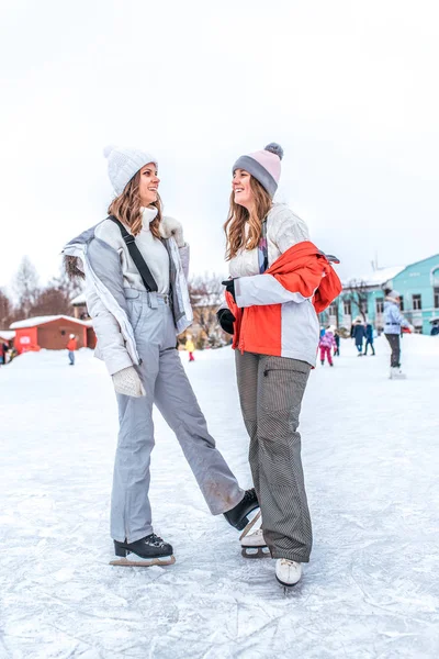 冬の2人のガールフレンドは、屋外で楽しい、暖かい冬の服の帽子を持っています。楽しい、スケート。冬の楽しさと屋外レクリエーションの喜びの感情。週末の休日に友達とおしゃべりする概念. — ストック写真