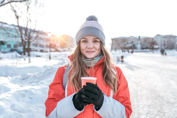 Close-up seorang gadis di musim dingin di luar. Dalam pakaian hangat, di tangan cangkir dengan minum teh kopi panas. Emosi kesenangan kesenangan dan rekreasi luar ruangan. Rambut panjang jaket musim dingin hangat dan topi . — Stok Foto