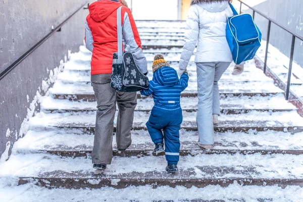 Keluarga muda adalah seorang anak laki-laki dan orang tua yang kembali ke rumah pada masa transisi di musim dingin di kota. Terhadap latar belakang salju dan tangga. Lihat dari belakang, pakaian musim dingin yang hangat dan tas bahu . — Stok Foto