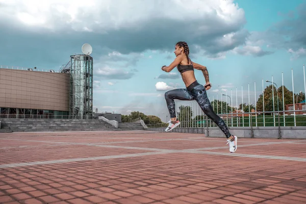 Menina muscular corre no verão na cidade, em uma corrida matinal, salto em altura. Top leggings Sportswear. Fones de ouvido. Fitness conceito jogging, estilo de vida. Espaço livre para texto . — Fotografia de Stock