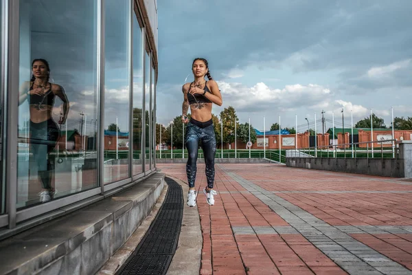 Menina muscular corre no verão na cidade, em uma corrida matinal, pele bronzeada, tatuagens. Top leggings Sportswear. Fones de ouvido. Fitness conceito jogging, estilo de vida. Espaço livre para texto . — Fotografia de Stock