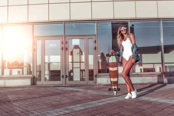 Schönes Mädchen, Sommer in der Stadt, glücklich lächelnd. Freiraum für Text. Skateboard Longboard weißer Body, Jeans. Konzept Mode Stil, Lifestyle. Emotionen der Freude und Entspannung. — Stockfoto