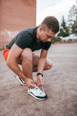 Erkek atlet koşucusu, temiz havada şehirdeki spor ayakkabılara ayakkabı bağcıkları bağlıyor. Fitness konsepti ve egzersiz, akıllı saat bilezik. Spor giyim t-shirt şort.