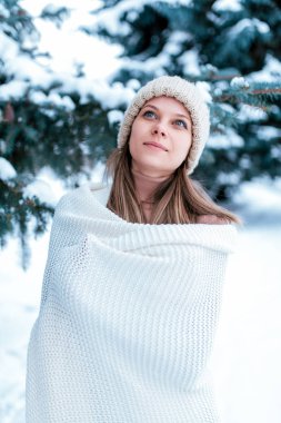 Woman in a white plaid, in the winter on the street, background snow drifts spruce. Happy smiling, looking to the sky. The concept of outdoor recreation on weekends, holidays at the resort.