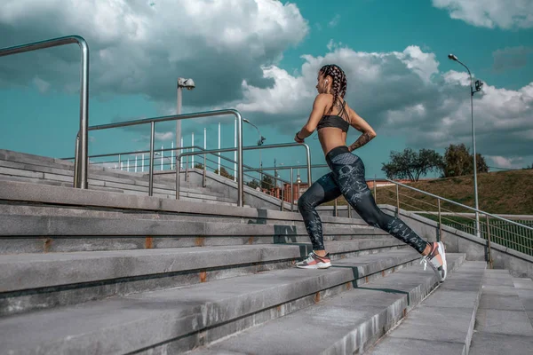 Mulher atleta, corre em escadas, na cidade de verão, espaço livre, treino de fitness, dia e manhã. Roupa de desporto, leggings top sneakers. Estilo de vida ativo, poder de motivação. Aplicação Internet, música . — Fotografia de Stock