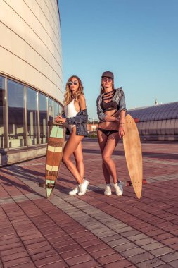 İki kız kız kız poz, arka plan bina, şehirde yaz aylarında yürüyüş, paten tahtası, rahat giyim şort mayo gömlek kavramı bir hafta sonu kaçamak, moda tarzı, modern yaşam tarzı.