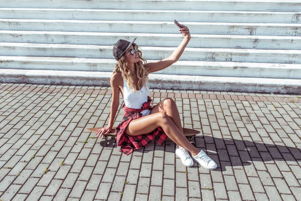 Frau Sommer Stadt weißen Körper. Skateboard schöne schlanke Figur, Sonnenbrille Turnschuhe. Fotos Telefon Online-Videoanruf Anwendung glücklich lächelnd. Konzept Mode Stil modernen Lebensstil. Freiraum. — Stockfoto