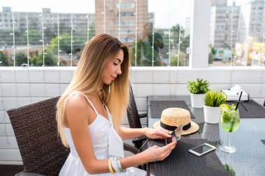 Kafede oturan bir kadın masa, el tableti, kulaklıkları. Müzik dinler, sosyal ağlarda mesaj yazar. Internet'e online başvuru. Güzel kız uzun saçlı. Restoranda yaz aylarında.