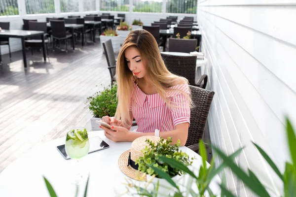 Жінка пише повідомлення в телефоні, влітку в кафе, рожеве плаття, відпочинок в ресторані. Сніданок обід на літній терасі. Онлайн-заявка в Інтернет соціальних мереж листування. — стокове фото