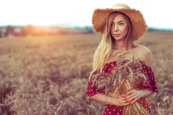 Seorang wanita dengan topi jerami gaun merah, di tangan memegang gandum telinga, ladang gandum musim panas. Ruang kosong. Konsep nutrisi sehat, produk ekologi di desa, bio gandum. Mengumpulkan roti produk alam . — Stok Foto