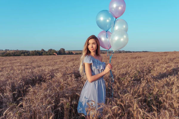 Young woman, in summer in a wheat field, with balloons. The concept of romance bye love, birthday party engagement. Emotions of joy, smiles, pleasure and outdoor recreation. Free space.