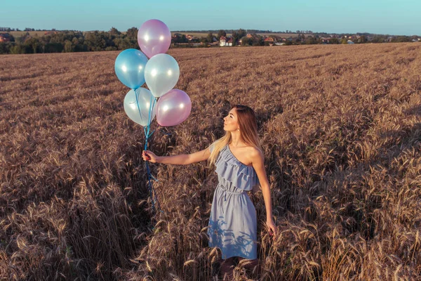 Young woman dress, summer wheat field, with balloons. Concept romance bye love, birthday party engagement. Emotions joy, smiles, pleasure outdoor recreation. Tanned figure long hair of girl.