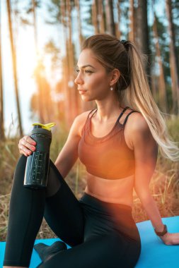 Kadın atlet egzersiz mat sonra dinlenme, fitness egzersiz yaz orman parkı. Aktif yaşam tarzı, spor tozluk üst. Protein veren su ile el kız çalkalayıcı, içki. Uzun saç tabaklanmış şekil.