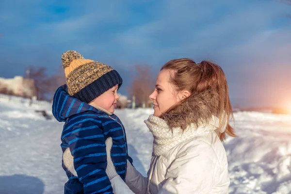 Vrouw moeder met kind winter stad, warme kleren, kleine jongen 3 jaar oud in blauwe jumpsuit en hoed. Ze praten over spelen, knuffelen, hebben plezier en ontspannen in het weekend in het resort, de achtergrond is sneeuw. — Stockfoto