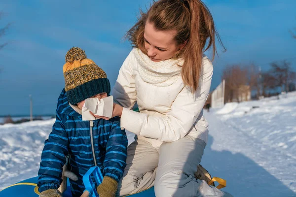 Moeder vrouw veegt haar kind s neus jongen 3 jaar oud, in de winter buiten, hoest snot, kou en griep, op een koude winterdag. Kamperen in het weekend op vakantie. — Stockfoto