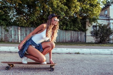 Kız kaykay, yaz şehir, arka plan yol asfalt ağaçları, longboard sürme. Boş alan. Denim spor ayakkabı beyzbol şapkası. Gençlik moda tarzı, modern eğlence trendi, tabaklanmış spor figürü.