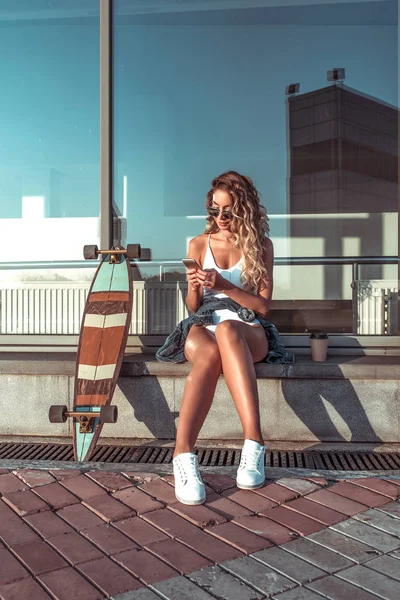 Summer city, woman writes message phone, online internet application, correspondence social networks. Reading news tapes smartphone. Skate longboard, long hair cup coffee tea. Free space for text.