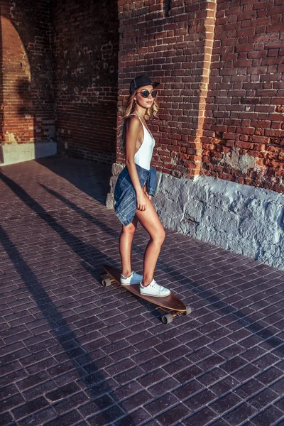 Gadis di musim panas naik skateboard, beristirahat di kota pada akhir pekan. Mode gaya muda, modern berani, gaya hidup berani. Concept walk rest emotion smile and lay woman in white bodysuit . — Stok Foto