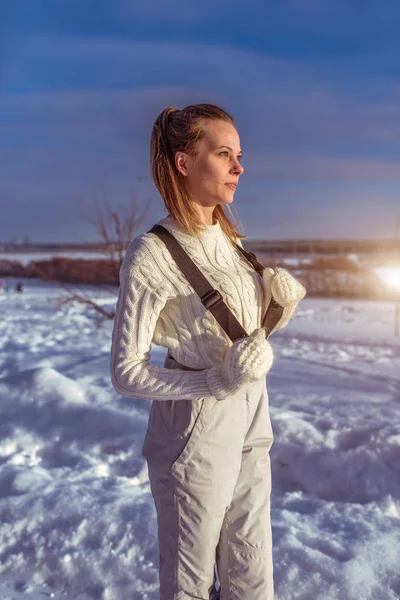 Nainen valkoisessa haalareita talvella ulkona, tausta on lumi ajelehtii, tarkastellaan etäisyys, lämmin villapaita ja valkoinen lapaset. Käsite ulkoilu viikonloppuna talven ulkopuolella . — kuvapankkivalokuva