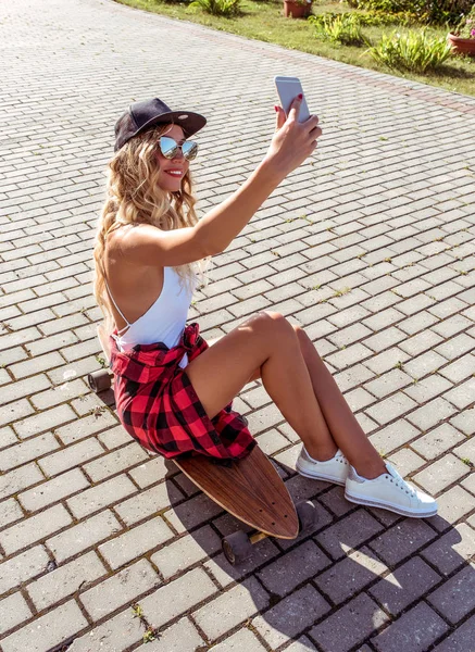 Una chica de skate, ciudad de verano, se hace selfies, llamada en línea a Internet. Feliz y sonriente longboard de pelo largo para montar. El estilo de vida de la juventud. Concepto ideas para una escapada de fin de semana — Foto de Stock