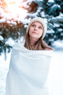 Bir portre yakın çekim kış kız arka plan kar Noel ağaçları. Beyaz sıcak kış şapka, büyük uzun yün ekose kazak. Tesiste soğuk havalarda, doğada hafta sonu dinlenin. Mutlu gülümsüyor.