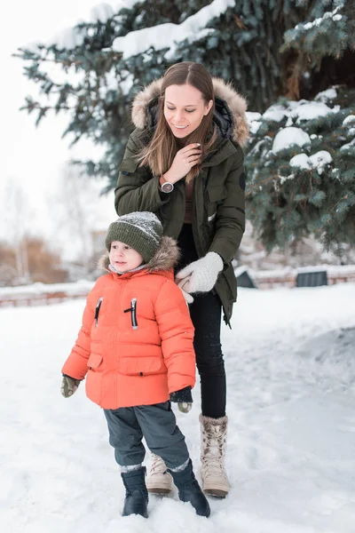 Junge Mutter, im Winter auf der Straße, geht mit ihrem kleinen Sohn einen Jungen von 3 Jahren. warme Jacke Winterkleidung. Ruhe am Wochenende Spaziergang an der frischen Luft, Hintergrund Schneebaum und Schneeverwehungen. — Stockfoto