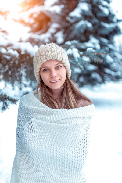 Das Mädchen im Winter steht lächelnd da, ruht sich an der frischen Luft im Wald aus. weißer Pullover kariert, warme Strickmütze. Emotionen der Freude Spaß Winterurlaub Genuss. Hintergrund Schnee vertreibt Bäume. — Stockfoto