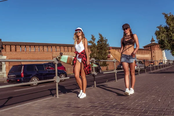 Dua pacar perempuan berjalan kota, latar belakang jalan raya skateboard mobil, indah dan kecokelatan angka. Menerima pacar teman baik. Istirahat akhir pekan, pakaian modern, gaya hidup fashion, tren . — Stok Foto