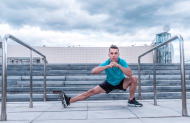 Erkek atlet, yaz aylarında şehirde, koşu öncesi kaslar germe, Fitness eğitim, spor, konsantrasyon ve hedefe odaklanmak. Merdiven arka plan ve mavi gökyüzü.