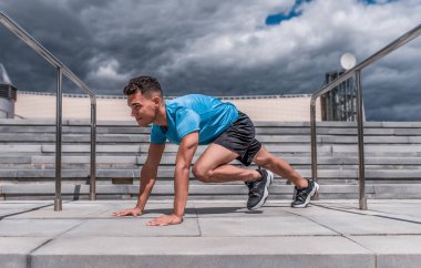 Bir adam bir atlet, abdominal egzersizleri, kaslar, şehirde yaz, jogging önce kaslar germe, Fitness eğitim, spor, konsantrasyon. Merdiven arka plan ve mavi gökyüzü.