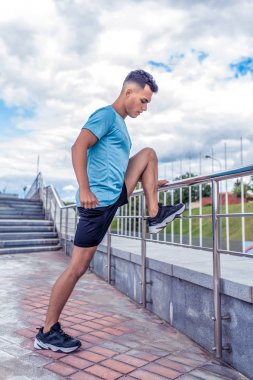 Erkek atlet bacak eğitim bacaklar kasları ısıtmak germe, yaz kentinde, jogging önce kaslar germe, Fitness eğitim, spor, konsantrasyon. Merdiven arka plan ve mavi gökyüzü.