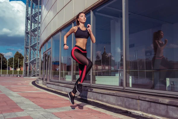 Szép fiatal lány, nyári délelőtti város fut futni, háttér üvegablakok épület, aktív életmód, fitness jellegű, szabad hely, sportruházat Leggings Top, cserzett alak. — Stock Fotó