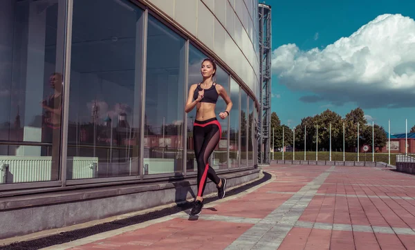 young beautiful woman jogging summer, morning in city, business lady, background glass windows building, active lifestyle, free space, sportswear leggings top figure. Clouds background, brick tile.