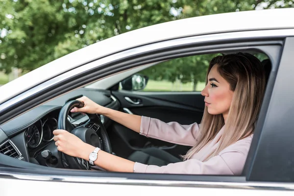 Mujer conduciendo un coche, pelo largo, mirada seria, en verano en el compartimiento de pasajeros de un coche blanco de clase business. La señora de los negocios va a trabajar . —  Fotos de Stock