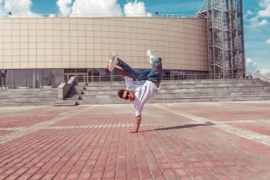 beyaz t-shirt genç adam dansçı, kot pantolon, bir kol üzerinde duruyor, yaz şehir, güneş gözlüğü, arka plan binası, aktif hip hop, gençlik yaşam tarzı, metin için boş alan, akrobatik dublör fren dans