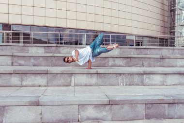 atlet adam beyaz t-shirt bir dansçı, kot pantolon, bir kol üzerinde duruyor, şehirde yaz aylarında, güneş gözlüğü, merdiven arka plan, aktif hip hop, gençlik yaşam tarzı, metin için boş alan, akrobatik hile break dans