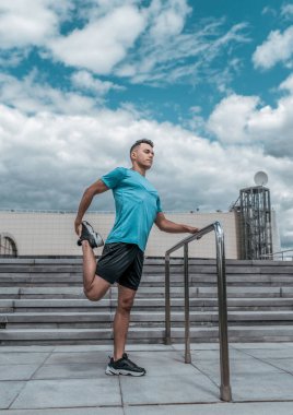 Atlet adam eğitim den önce diz ve bacak kas germe yapıyor. Şehirde yaz aylarında, bir koşu fitness egzersiz için hazırlanıyor, spor şort t-shirt ve spor ayakkabı. Adım bulut arka plan.