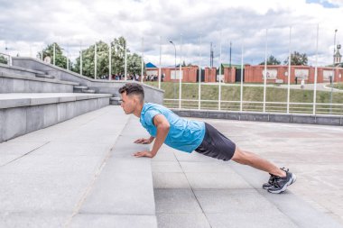 Erkek atlet şehirde yaz aylarında merdivenlerden iterek, kas eğitimi. Aktif yaşam tarzı, fitness motivasyonu, şehirde egzersiz. Spor Giyim T-shirt Spor Ayakkabı.