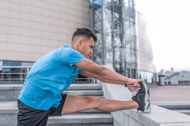 Atletik adam çalışan, bacak kasları ısınma, eğitim öncesi, şehirde yaz aylarında, spor t-shirt şort, spor ayakkabı, bir çalışma sabah fitness.