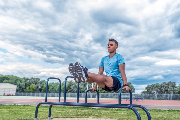 Male athlete, summer city, background clouds grass sport playground. Abdominal muscle training, difficult exercise, corner. Active lifestyle young people, workout nature. Free space text. Motivation.